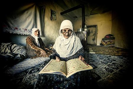The old woman is reading the Koran.