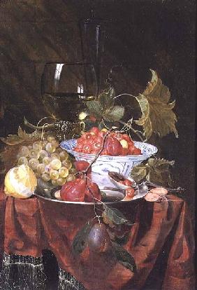 Still life with wild strawberries, plums, grapes and a lemon on a draped ledge