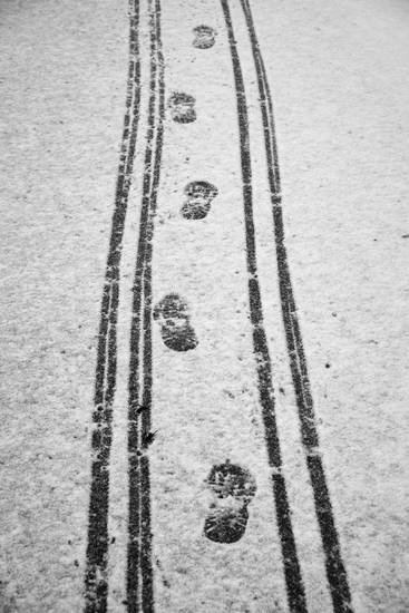 Verschiedene Reifenspuren und Fußspuren auf der Schneefahrbahn